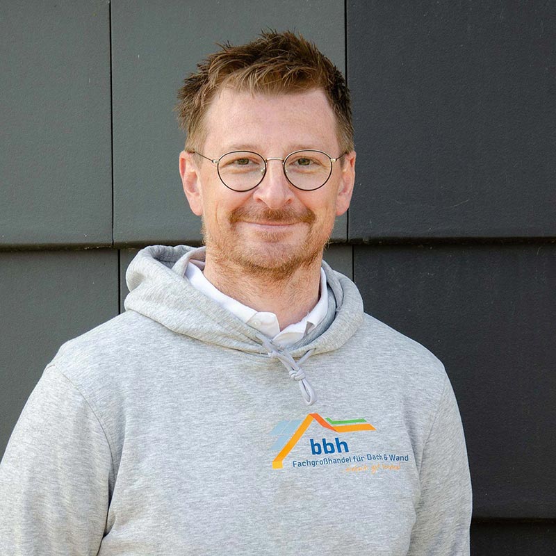 Jan-Niklas Bergemann Mann mit Brille und grauem Hoodie mit bbh-Logo vor dunkler Wand
