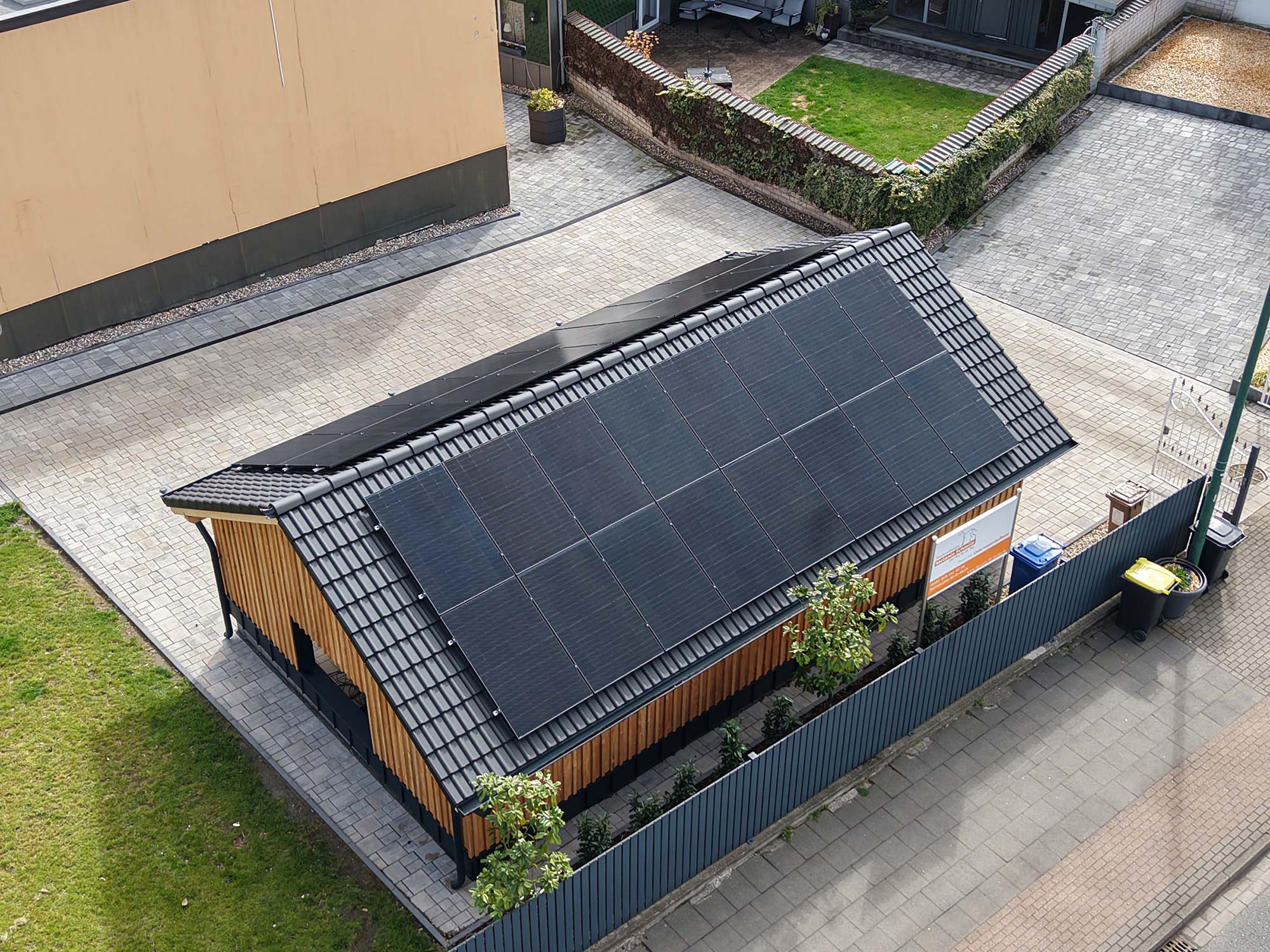 Photovoltaik für Ihr Dach Haus mit schwarzem Dach, das vollständig mit Solarmodulen bedeckt ist, umgeben von Zaun und Grünfläche.